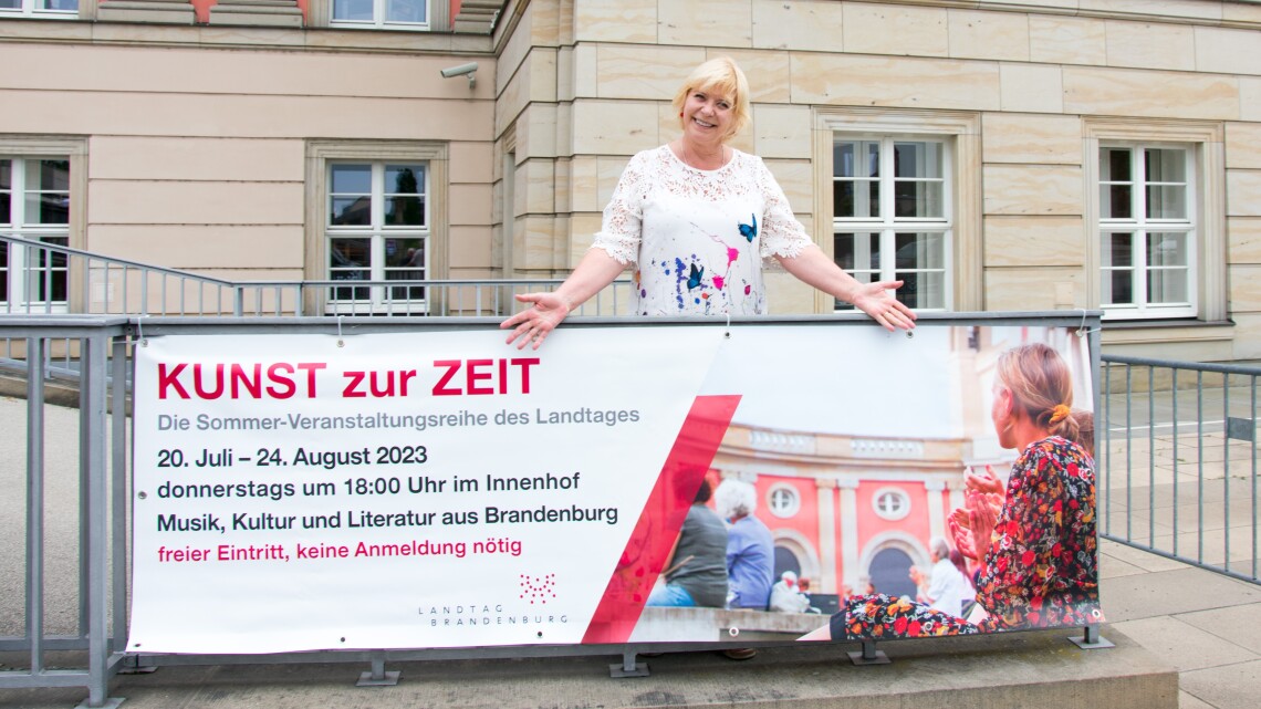 Landtagspräsidentin Prof. Dr. Liedtke entrollt ein Werbebanner für die Reihe KUNST zur ZEIT.